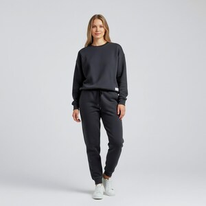 May include: A charcoal gray sweatshirt and matching sweatpants set. The crew neck sweatshirt has a small white tag on the side. The sweatpants have a drawstring waist and cuffed ankles. The person is wearing white sneakers.