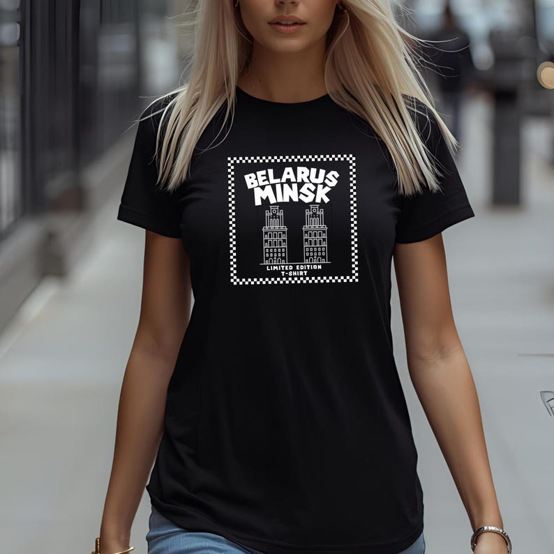 May include: Black t-shirt featuring a white graphic design with the text "BELARUS MINSK" and illustrations of buildings. The design is framed by a checkered border. The text "LIMITED EDITION T-SHIRT" is below the buildings.