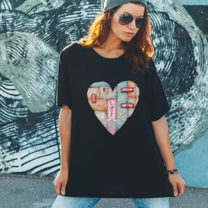 Puede incluir: Camiseta negra con un diseño en forma de corazón compuesto por elementos de madera y la palabra "LOVE". El diseño del corazón incorpora varios colores y texturas, creando un aspecto único y artístico. La camiseta es una prenda casual.
