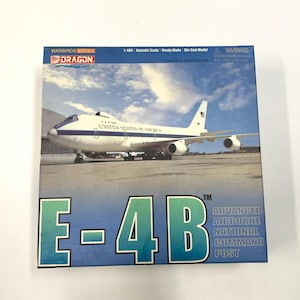 May include: A die-cast model box featuring a white and blue E-4B aircraft, labeled "United States of America." The box has the text "WARBIRDS SERIES" and "E-4B ADVANCED AIRBORNE NATIONAL COMMAND POST."