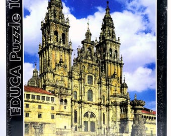 Può includere: Un puzzle da 1000 pezzi con un'immagine dettagliata di una cattedrale con più guglie e dettagli architettonici. La scatola del puzzle ha il testo "EDUCA Puzzle 1000" sul lato e un bordo nero.