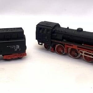 May include: A two-part model train set. The train is black with red wheels and detailing. The locomotive has a detailed design, and the tender is a separate piece. The set is designed to resemble a vintage steam engine.