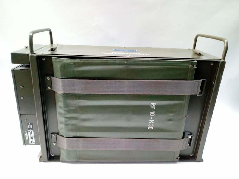 Peut inclure: Bo&icirc;te m&eacute;tallique vert olive de style militaire avec deux poign&eacute;es sur le dessus. La bo&icirc;te a une forme rectangulaire avec un insert en tissu vert fix&eacute; par deux sangles grises. Le texte "RF 10-K 30" est visible.