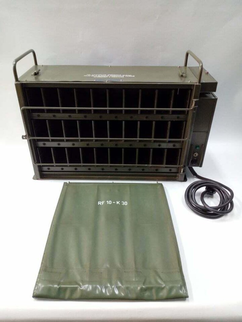 Peut inclure: Un appareil m&eacute;tallique vert olive avec une fa&ccedil;ade grillag&eacute;e et deux poign&eacute;es sur le dessus. Une housse assortie vert olive avec le texte "RF 10-K 30" est devant l'appareil. Un cordon d'alimentation noir est connect&eacute; &agrave; l'appareil.