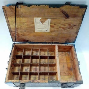 May include: Open wooden box with a hinged lid, featuring a divided interior with small compartments and a larger section. The box is made of light-colored wood with visible grain, and has metal latches and hinges. The exterior has blue and black paint.