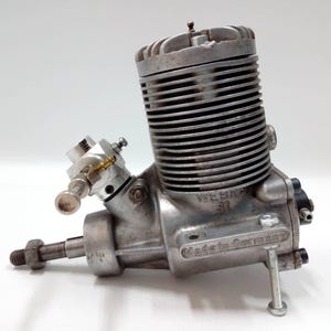 May include: A silver model engine with a ribbed cylinder and various mechanical parts. The engine is marked "WEBRA 91" and "Made in Germany". The engine is designed for model aircraft or similar applications.