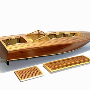 Pode incluir: Um modelo de lancha em madeira com casco de mogno polido, cockpit aberto com para-brisas e dois painéis de convés de madeira ripada separados colocados à frente da embarcação. O barco tem uma proa pontiaguda e uma popa plana com um leme preto.