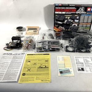 May include: A Tamiya Tractor Truck Multi-Function Control Unit model kit, with various components, including a speaker, circuit boards, and instruction manuals. The box features a graphic of a semi-truck.