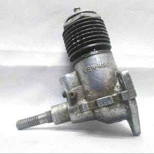 May include: A vintage silver-toned model engine with the text "WEN-MAC" visible. The engine features a ribbed cylinder head and a threaded shaft. The engine is likely for a model airplane or car.