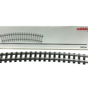 May include: Curved model train track set with a white box. The box has a diagram of the track and the Märklin logo. The track is dark gray and has a curved design. The box has the number 59230.