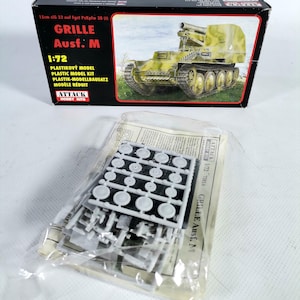 Op de afbeelding: Een modelbouwdoos en niet-gemonteerde onderdelen. De doos toont een illustratie van een militair voertuig met een groot kanon, met het opschrift "GRILLE Ausf. M" en "1:72". De kit bevat plastic sprues met kleine, gedetailleerde componenten.