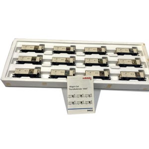 Puede incluir: Un conjunto de doce vagones de tren modelo en miniatura en una bandeja blanca. Cada vagón es de color beige con detalles en negro y un diseño impreso. Se incluye un folleto pequeño con el texto "Wagen-Set 'Kunstkalender 1998'".