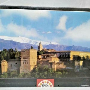 Op de afbeelding: Een puzzel van 1000 stukjes met een schilderachtig uitzicht op een historisch kasteelcomplex met een berglandschap onder een blauwe lucht. De puzzeldoos heeft de tekst "EDUCA Puzzle 1000".
