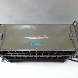 Peut inclure: Un appareil m&eacute;tallique vert olive de forme rectangulaire, avec une fa&ccedil;ade en grille et deux poign&eacute;es arqu&eacute;es. La surface sup&eacute;rieure comporte du texte et une &eacute;tiquette bleue. Un c&acirc;ble d'alimentation noir sort du c&ocirc;t&eacute; droit.