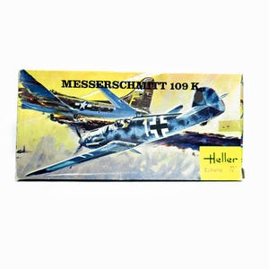 May include: A model kit box featuring a Messerschmitt 109 K aircraft illustration. The box has a yellow background with images of two blue and gray airplanes. The text "Messerschmitt 109 K" is displayed at the top.