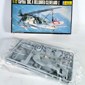 Op de afbeelding: Een modelbouwpakket van een Curtiss SBC-4 Helldiver/Cleveland I vliegtuig. De doos toont een gedetailleerde illustratie van het vliegtuig in vlucht. De kit bevat ongebouwde plastic onderdelen in een transparante zak.
