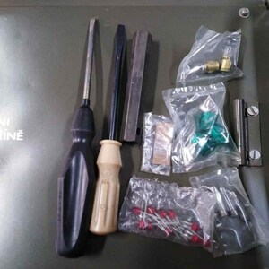 Peut inclure: Ensemble d'outils et de composants mat&eacute;riels, comprenant des tournevis, des barres m&eacute;talliques et de petites pi&egrave;ces dans des sachets en plastique transparent. L'ensemble est dispos&eacute; sur une surface verte.