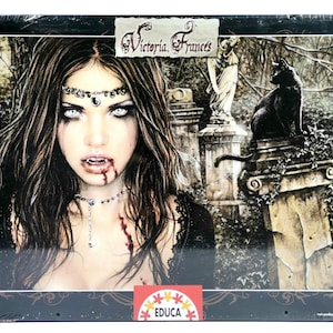 May include: A 1000-piece puzzle featuring a gothic illustration by Victoria Frances. The image depicts a vampire woman with white eyes and blood on her face, a black cat, and a statue in a graveyard setting.