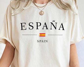 Könnte beinhalten: Cremefarbenes T-Shirt mit dem Wort "ESPAÑA" in schwarzen Großbuchstaben. Darunter ein waagerechter Strich, die spanische Flagge und das Wort "SPAIN". Das T-Shirt wird getragen.