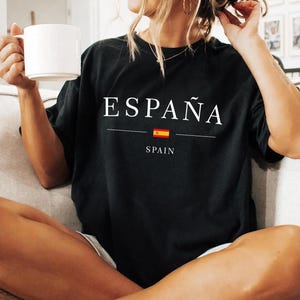 May include: Black t-shirt with the word "ESPA&Ntilde;A" in white, above a horizontal line, a small Spanish flag, and the word "SPAIN". The shirt is a dark color and has a relaxed fit.