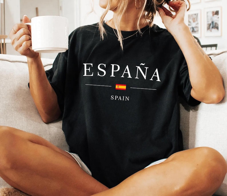 May include: Black t-shirt with the word "ESPA&Ntilde;A" in white, above a horizontal line, a small Spanish flag, and the word "SPAIN". The shirt is a dark color and has a relaxed fit.