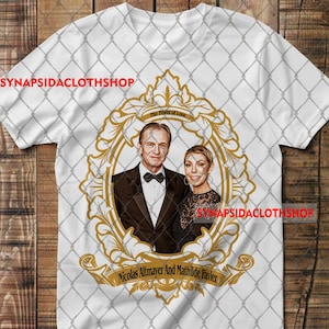 以下が含まれることがあります： 中央に金色の装飾的なフレームが施された白いTシャツ。フレーム内にはスーツ姿の男性と黒いトップスを着た女性のポートレートが描かれています。フレームのデザイン内には「The Power of Love」および「Nicolas Altmayer And Mathilde Favier」というテキストが印刷されています。