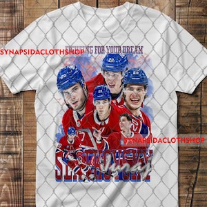 Könnte beinhalten: Ein weißes T-Shirt mit einem Grafikdruck eines Eishockeyspielers mit blauem Helm und rotem Trikot in verschiedenen Posen. Der Text "FIGHTING FOR YOUR DREAM" steht oben und der Name "Slafkovsky" ist unten in Schreibschrift aufgedruckt.