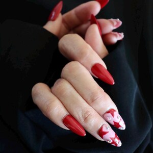 Peut inclure: Gros plan sur des mains avec de longs ongles en amande rouges. Certains ongles ont un motif géométrique rose et rouge avec des strass.