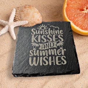 May include: Black slate coaster with the text "Sunshine Kisses and Summer Wishes" in white lettering. The coaster is surrounded by sand, a seashell, and a slice of grapefruit.