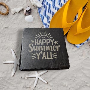 May include: Black slate coaster with the text "HAPPY Summer Y'all" in gold lettering. The coaster is on a white sandy beach with seashells and flip flops.
