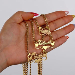 Peut inclure: Colliers dorés avec chaînes gourmettes. Chaque collier porte un nom différent : "Frances", "Belinda" et "Caroline", dans une police décorative. Les pendentifs comportent des motifs de cœur et de couronne.