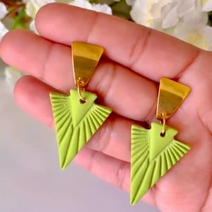 Puede incluir: Un par de pendientes triangulares verdes con detalles dorados. Los pendientes tienen un diseño geométrico con líneas que irradian desde el centro.