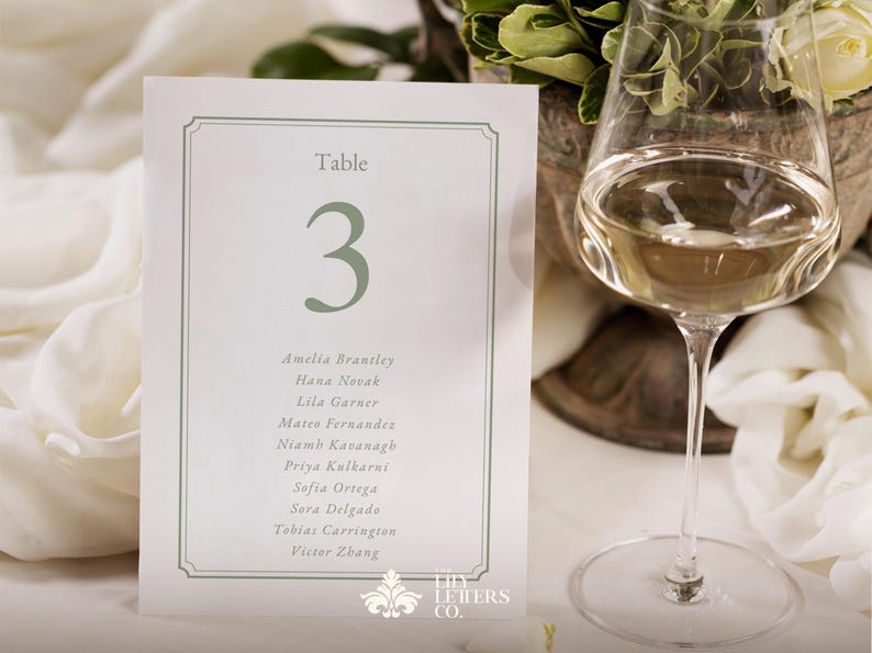 May include: A white table card with a green border and the number 3 in green. The card lists names below the number. A wine glass with white wine is in the background.