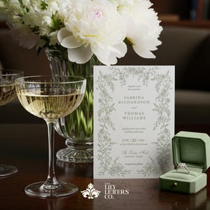 Puede incluir: Una invitaci&oacute;n de boda con dise&ntilde;o floral, champ&aacute;n en dos copas y un anillo en una caja verde. La invitaci&oacute;n dice "Sabrina Richardson y Thomas Williams" con la fecha 20 de junio de 2026. Un jarr&oacute;n de flores blancas est&aacute; en el fondo.