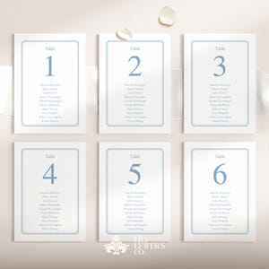 May include: Six white table cards with blue text and borders. Each card is labeled with a table number from one to six. The cards display guest names. The Lily Letters Co. logo is at the bottom.