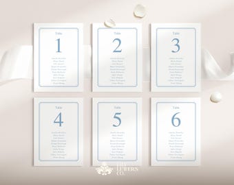 May include: Six white table cards with blue text and borders. Each card is labeled with a table number from one to six. The cards display guest names. The Lily Letters Co. logo is at the bottom.