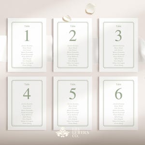 May include: Six white table number cards with sage green text and borders. Each card is labelled with a number from one to six, and includes a list of names. The cards are arranged on a light pink background with a white ribbon and decorative elements.