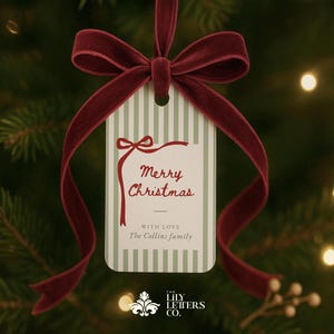 Może przedstawiać: Świąteczna etykieta na prezent z bordową aksamitną wstążką. Etykieta ma zielono-białe paski z napisem "Merry Christmas" w ozdobnej czcionce. Etykieta zawiera również tekst "With Love, The Collins family."