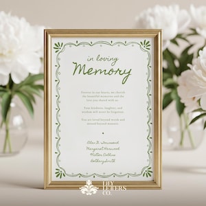 May include: A gold framed memorial sign with green script reading "in loving Memory". The sign has a decorative green border and text about cherished memories. White peonies in glass vases are in the background.