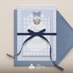 May include: Baby shower invitation set with a blue gingham pattern, a teddy bear graphic, and a navy blue velvet ribbon. The invitation includes the text "Diaper Raffle" and other details.