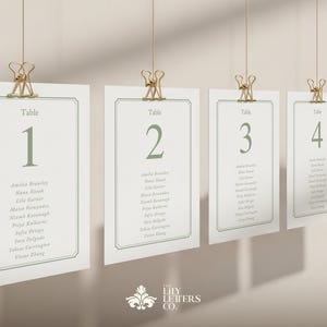 May include: Several hanging table cards numbered 1 to 5 in a soft green. Each card, held by a gold clip, displays names. The cards are for a wedding or event, with a decorative border.