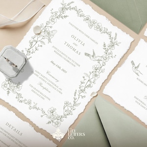 May include: Wedding invitation suite featuring a ring in a gray velvet box, invitation cards, and envelopes. The invitation has floral and hummingbird illustrations, with the names Olivia and Thomas, and the date May 15th, 2025.