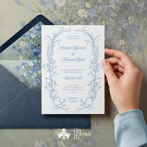 May include: A blue and white wedding invitation with a floral border. The invitation reads "Together with their families Olivia Mitchell & Thomas Scott.  May 19th, 2025. Villa Amore, Pavilla, California.  Reception to follow."