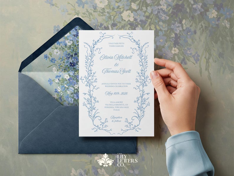 May include: A blue and white wedding invitation with a floral border. The invitation reads "Together with their families Olivia Mitchell & Thomas Scott.  May 19th, 2025. Villa Amore, Pavilla, California.  Reception to follow."