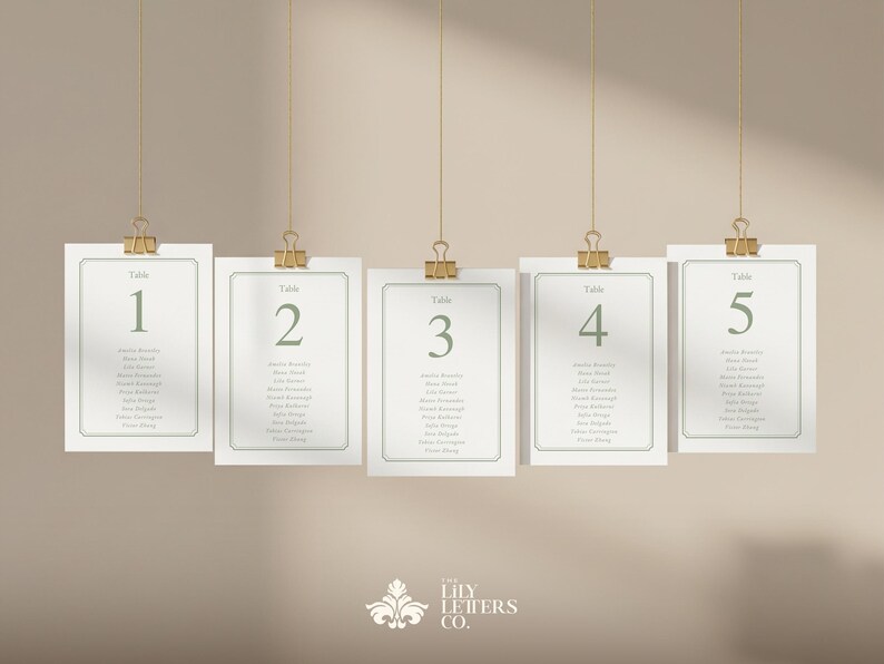 May include: Five rectangular cards with green text, each labelled with a table number from 1 to 5. The cards are suspended by gold clips and strings against a neutral background. Each card lists names.