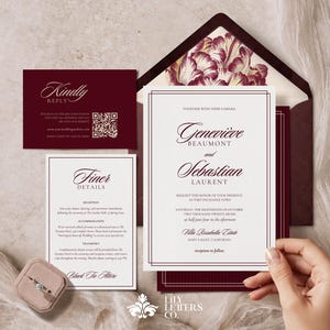 May include: Elegant wedding invitation suite in burgundy and white. Includes invitation, RSVP, details card, and envelope with floral lining. A ring box with a diamond ring is also present. The invitation features the names Geneviève and Sebastian.