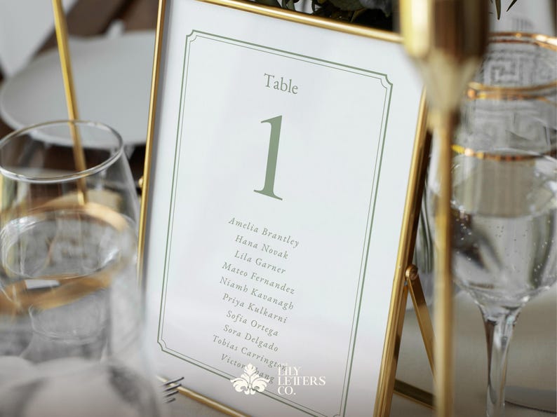 May include: A framed table number one with a gold border. The table number is in a light green colour, with a list of names below. The frame is set on a table with a glass of water and a gold candle holder.