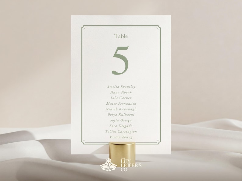May include: A wedding table number card with the number 5 in green, and a list of names. The card is held by a gold-coloured cylindrical holder. The text "Table" is at the top.