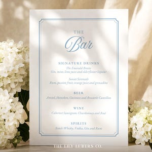 May include: A white rectangular bar menu sign with a light blue border and elegant blue text. The sign features the heading The Bar, followed by sections for Signature Drinks, Beer, Wine, and Spirits, with specific drink names listed below.
