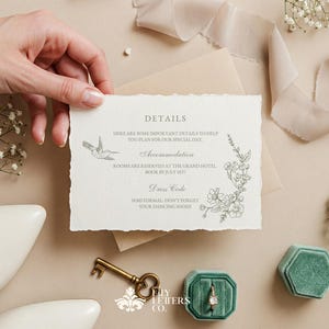 May include: A wedding invitation with torn edges, featuring floral and hummingbird illustrations. The invitation is held by a hand, with a key, ring box, and shoes in the background. The text on the invitation reads "DETAILS".
